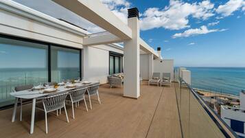 Ein Balkon mit einem Esstisch für vier Personen, zwei Liegestühlen und Meerblick.
