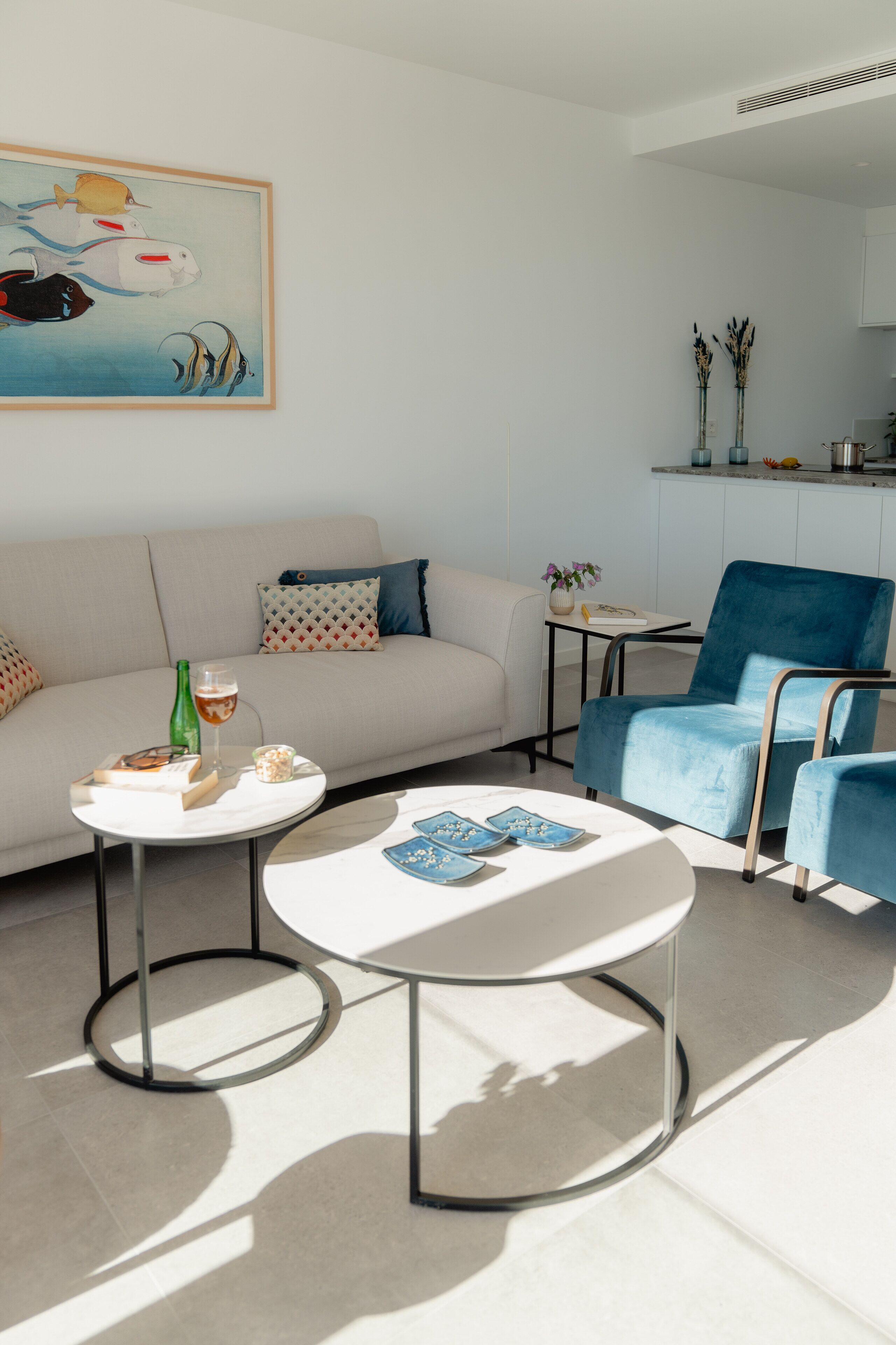 Uma sala de estar moderna com um sofá, uma poltrona azul, uma mesa de centro e um quadro na parede.