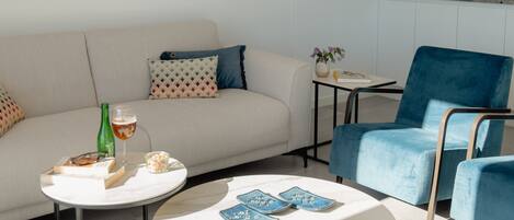 Uma sala de estar moderna com um sofá, uma poltrona azul, uma mesa de centro e um quadro na parede.