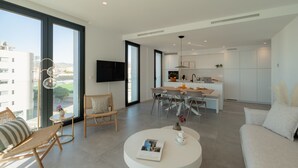 A modern living room with a round coffee table, a sofa, and a dining area with chairs and a kitchen in the background. - Horizonte Line (Villajoyosa)