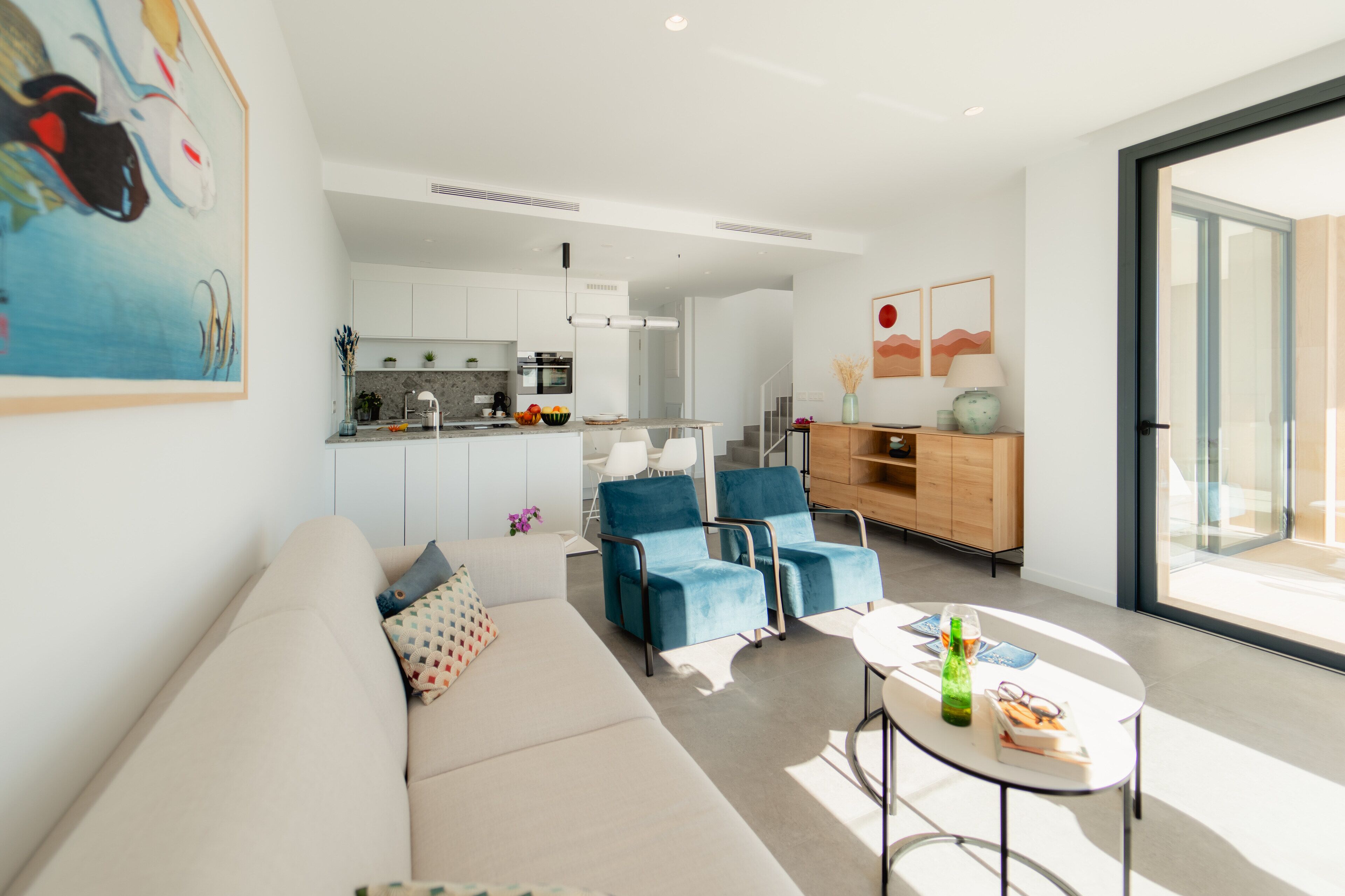 A modern living room with a sofa, two blue armchairs, a coffee table, and a kitchen in the background.