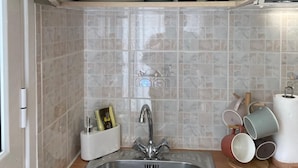 A kitchen with a stainless steel sink, a white cabinet with dishes, and a microwave. - Stefanos Home - Apartment 1 (Kefalonia)