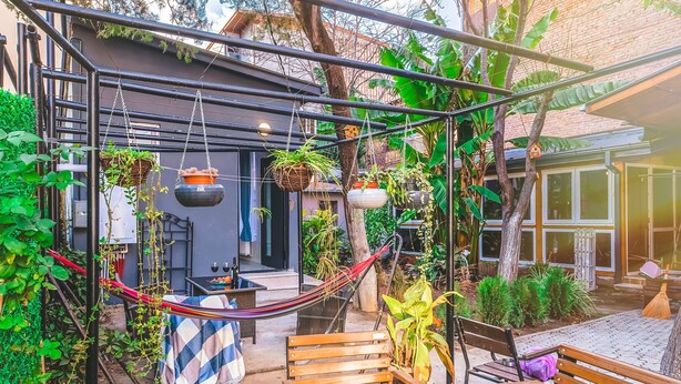 A cozy outdoor seating area with wooden benches, a hammock, and hanging planters. - HB apartments Aghmashenebeli III (Tbilisi)