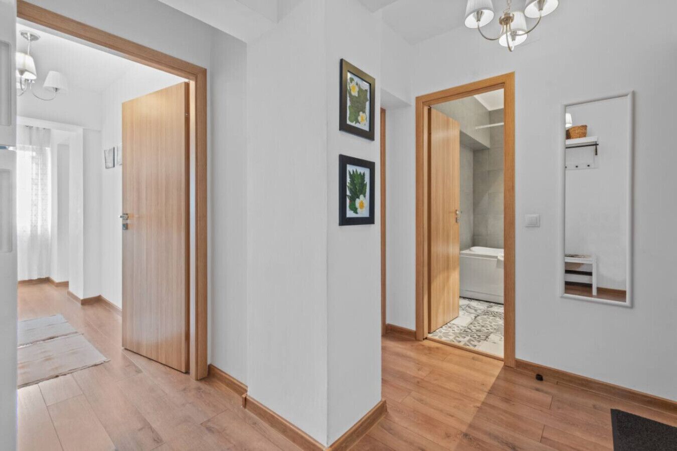A hallway with wooden flooring, a wooden door, and a bathroom visible through an open door.