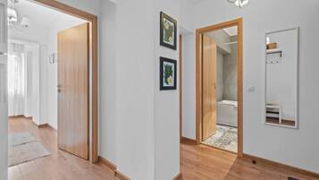 A hallway with wooden flooring, a wooden door, and a bathroom visible through an open door.