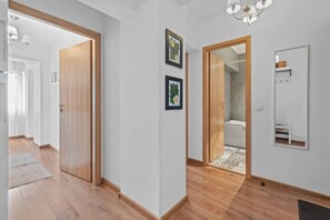 A hallway with wooden flooring, a wooden door, and a bathroom visible through an open door.