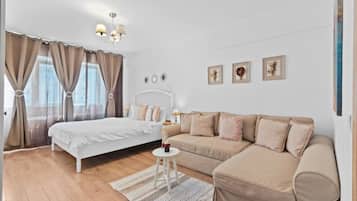A bedroom with a bed, a sofa, a small table, and a chandelier.