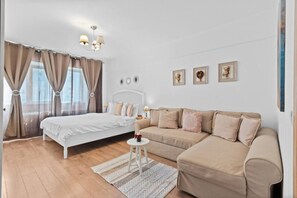 A bedroom with a bed, a sofa, a small table, and a chandelier.