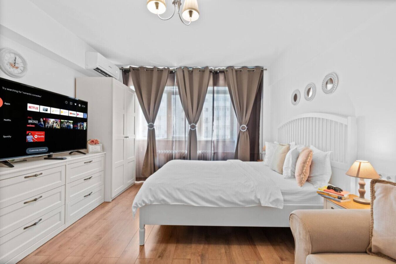 Un dormitorio moderno con cama, televisión, cómoda y ventana con cortinas.