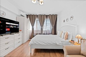 Een moderne slaapkamer met een bed, een televisie, een dressoir en een raam met gordijnen.