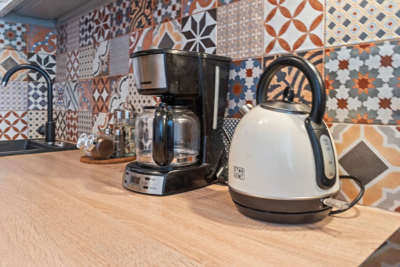 A kitchen with a coffee maker, kettle, and a glass container on the counter.