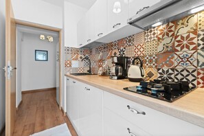 A compact kitchen with a tiled backsplash, a coffee maker, a kettle, and a sink.