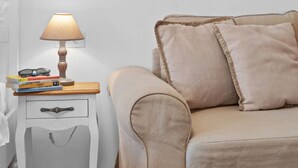 A bedroom with a beige sofa, a bedside table with a lamp, and a stack of books.