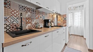A modern kitchen with a patterned backsplash, a black sink, and a coffee maker.
