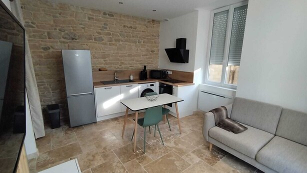 A compact kitchen with a dining area, a sofa, and a stone wall. - Appartement Lumineux en Rdc, Pour Séjour Touristique ou Professionnel (Bourgoin-Jallieu)