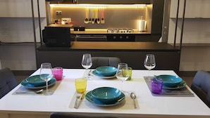 A modern dining area with a table set for four, featuring teal and blue plates, clear wine glasses, and colorful water glasses.