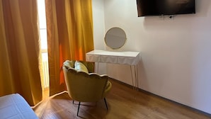 A room with a bed, a vanity with a mirror, a television on the wall, and a chair.