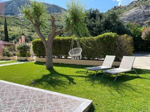 Un jardín con una silla hamaca, dos sillones y una zona de patio con baldosas.
