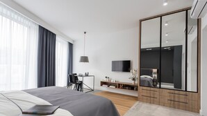 Een moderne hotelkamer met een groot bed, een bureau met stoel, een televisie, een kledingkast en een groot raam met gordijnen.
