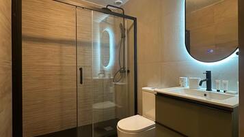 Un baño moderno con ducha de mampara, inodoro y tocador con espejo.