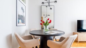 A modern dining area with a round table, four chairs, a vase with red tulips, and a flat-screen TV on a wooden cabinet. - López de Hoyos II (Madrid)