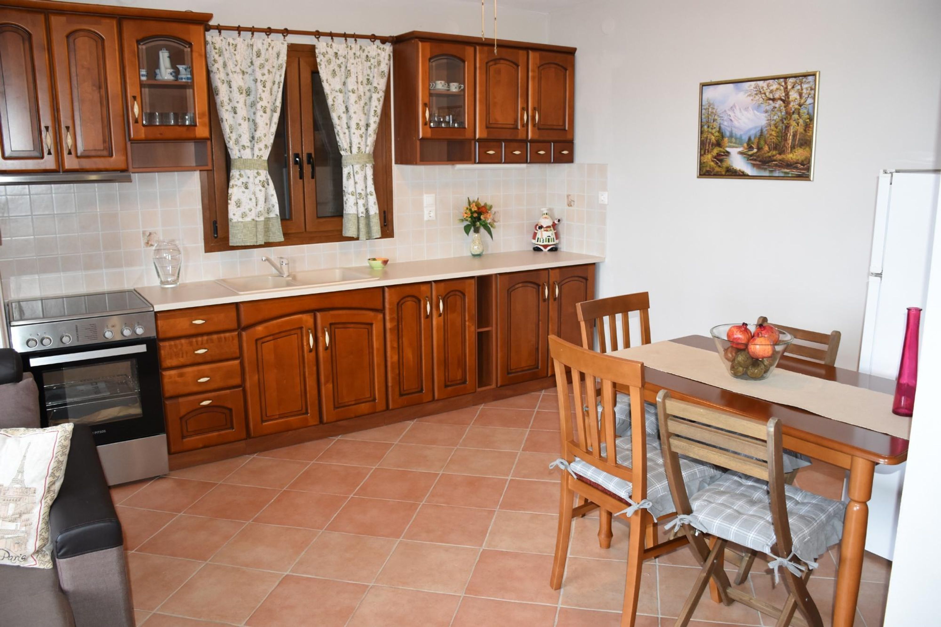 Une cuisine avec des meubles de rangement en bois, une table à manger avec des chaises, un réfrigérateur et un tableau accroché au mur.