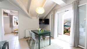 Un coin repas avec une table et des chaises, un téléviseur fixé au mur et une vue sur un navire par la fenêtre.