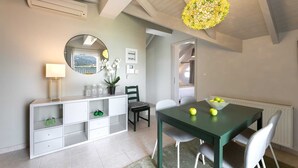 Un espace repas moderne avec une table verte et des chaises blanches, une console blanche avec un miroir et un lustre jaune à motifs floraux.