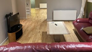 Un salon avec un canapé en cuir rouge, une table basse blanche, un téléviseur posé sur un meuble en bois et un radiateur blanc.
