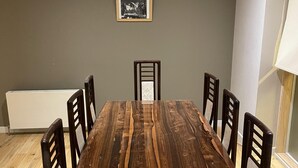 Une salle à manger avec une longue table en bois, six chaises, un radiateur et un tableau encadré au mur.