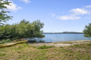 Un lago tranquilo con una canoa en la orilla, rodeado de árboles y un cielo despejado.