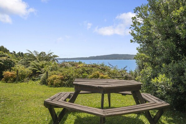 Una mesa de picnic de madera en un área verde con vistas a un cuerpo de agua y colinas al fondo.