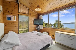 Habitación con paneles de madera, una cama, un televisor, un aparador y una ventana con vista al mar.