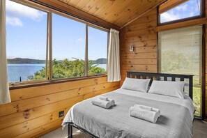 Un dormitorio tipo cabaña de madera con una cama, una ventana con cortinas y vistas a un lago.