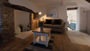A cozy living room with a stone wall, a wooden coffee table, a sofa, and a kitchen in the background. - Cosy Central Townhouse in Woodstock (Woodstock)