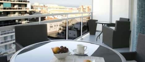 A balcony with a round table, a bowl of fruit, a cup, and a plate of pastries.