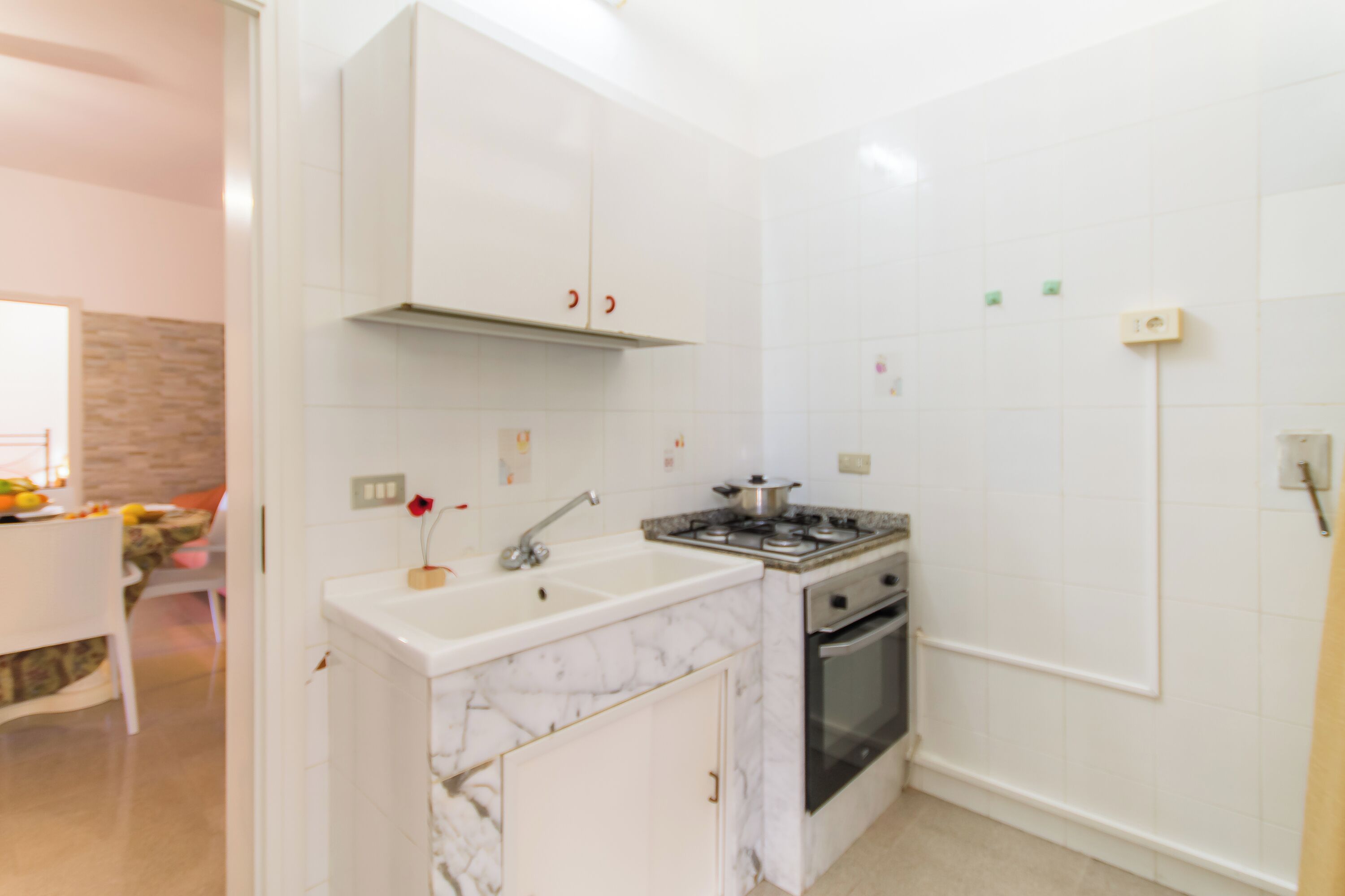 A compact kitchen with white cabinets, a marble sink, a stove, and an oven.