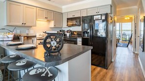 A modern kitchen with a central island, stainless steel appliances, and a bar area with stools. - Jolly Roger (North Topsail Beach)