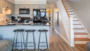 A modern kitchen with a central island, bar stools, and a staircase leading to a lofted area. - Jolly Roger (North Topsail Beach)