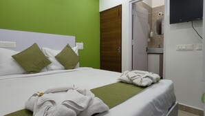 A hotel room with a bed, green pillows, a green towel, and a TV mounted on the wall. - Athulya Stays (Bengaluru)