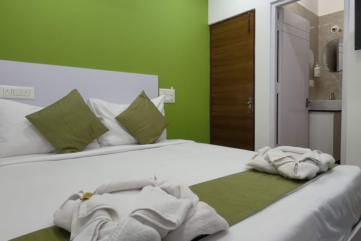 Una habitación de hotel con una cama, almohadas verdes, una toalla verde y un televisor montado en la pared.