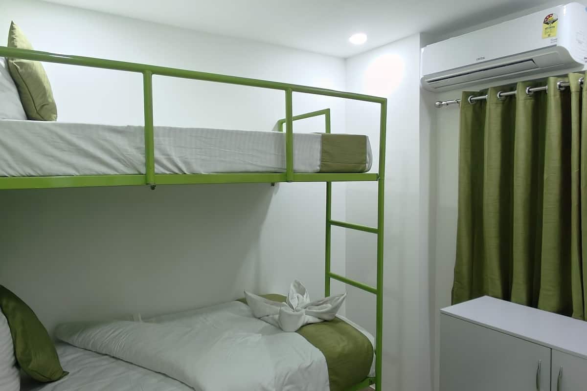 Habitación con literas de estructura verde, ropa de cama blanca y una cortina en la ventana.