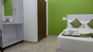 Quarto de hotel com uma cama, paredes verdes, um guarda-roupa e uma toalha verde sobre a cama.