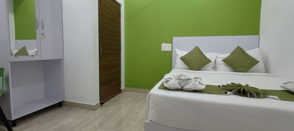 Habitación de hotel con cama, paredes verdes, un armario y una toalla verde sobre la cama.