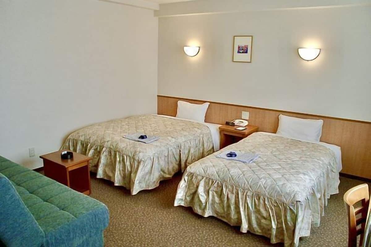 Quarto de hotel com duas camas, uma escrivaninha pequena, uma cadeira e um sofá.