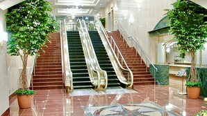 A lobby with two escalators, a star-shaped floor design, and potted plants. - Yonago Universal Hotel  (Yonago)