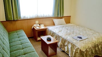 A hotel room with a single bed, a small bedside table with a phone and notepad, a green sofa, and a window with curtains.