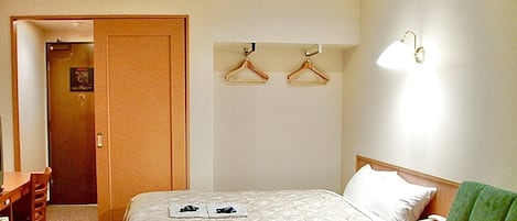 A hotel room with a bed, a desk, a chair, a bedside table, and a hanging light fixture.