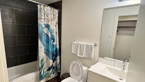 A bathroom with a bathtub, toilet, sink, and a shower curtain with a blue and white design. - Dt 1Bed 1bath Cozy Suite 8 Min Walk To Arena (Edmonton)