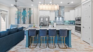 A modern kitchen with a central island, bar stools, and a ceiling fan. - 30A | Gorgeous Home | Resort Pool (Rosemary Beach)